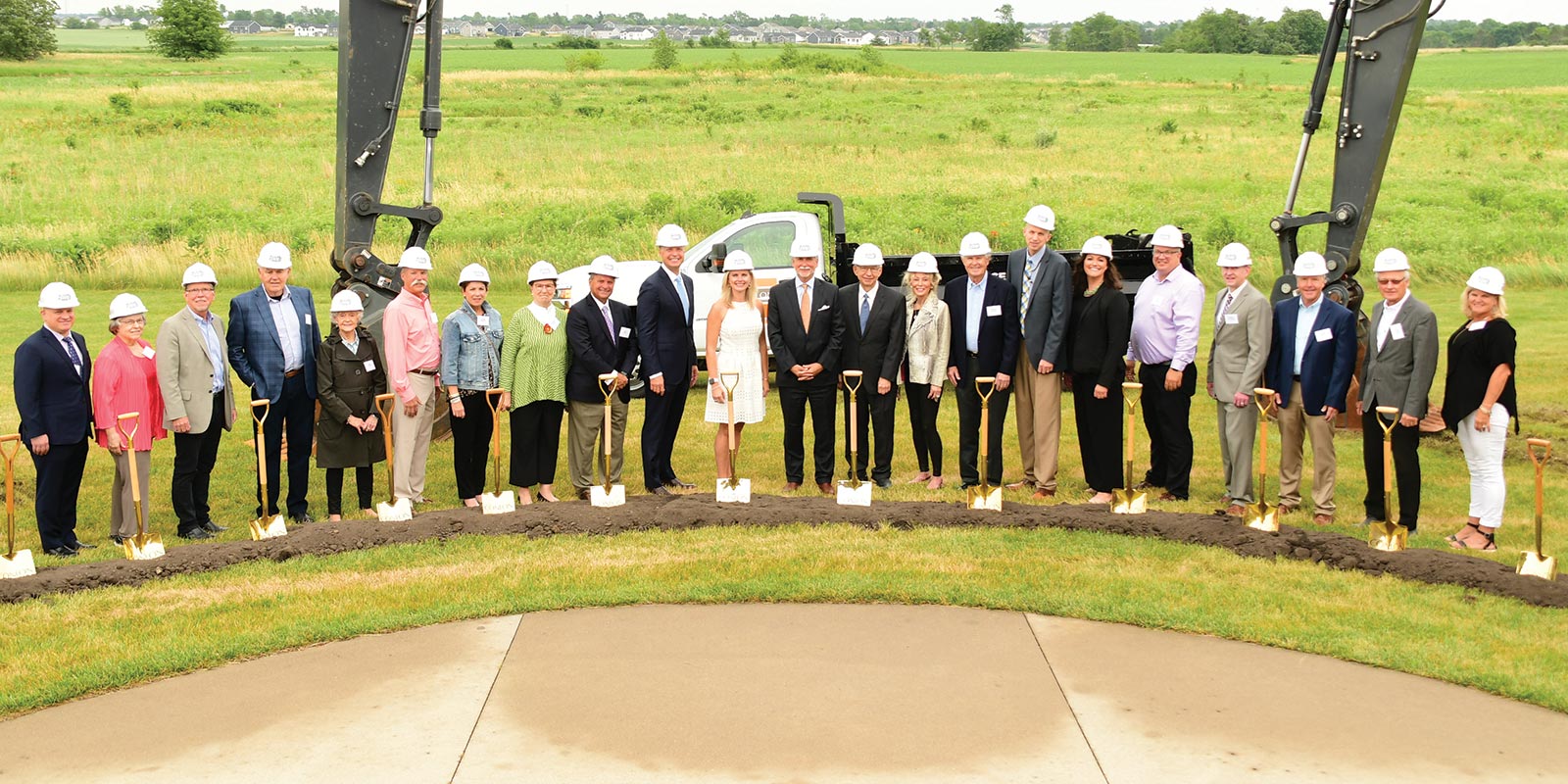 A group of buisiness people with hard hats and shovels at a worksite